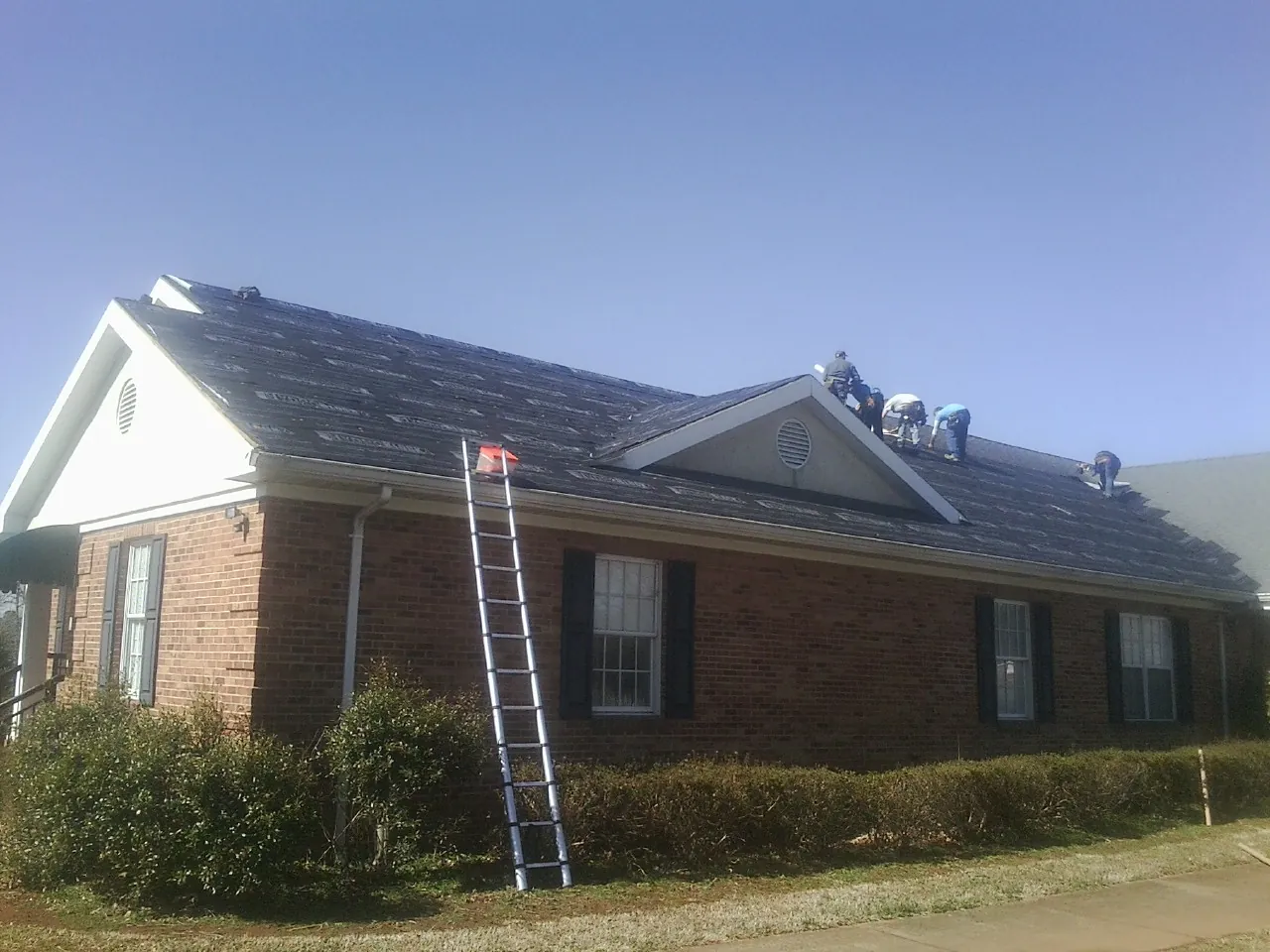 Crew tearing shingles off a brick ranch roof with a ladder set — Emergency Roof Repair work by our crew in Dunfermline