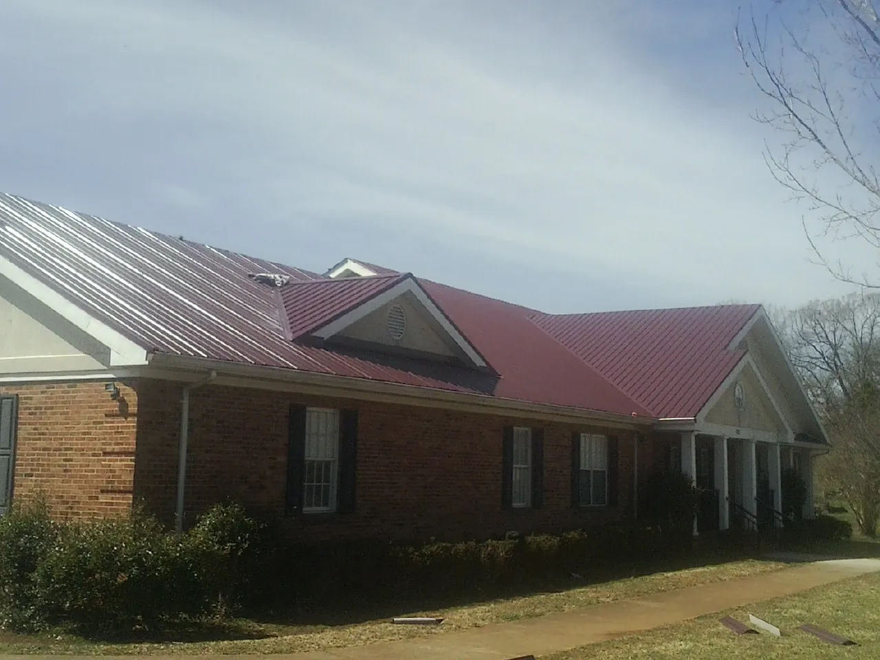 Red metal roof with gabled entries on a long brick building, from a Hail Damage Roof Repair job in Dunfermline