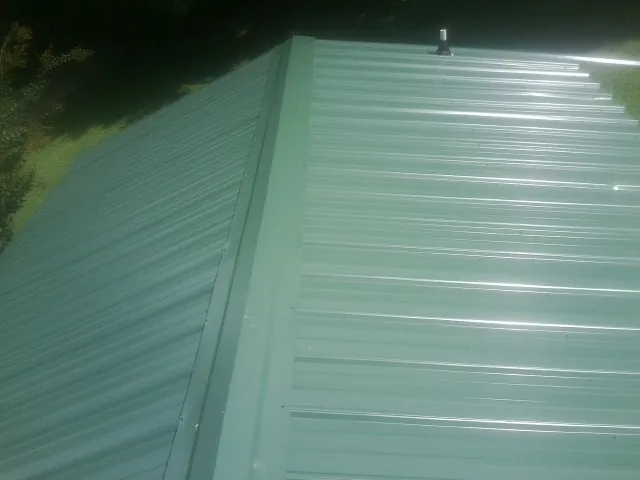 New green metal panels meeting at the ridge of a roof — Flat Roof Repair work by our crew in Dunfermline