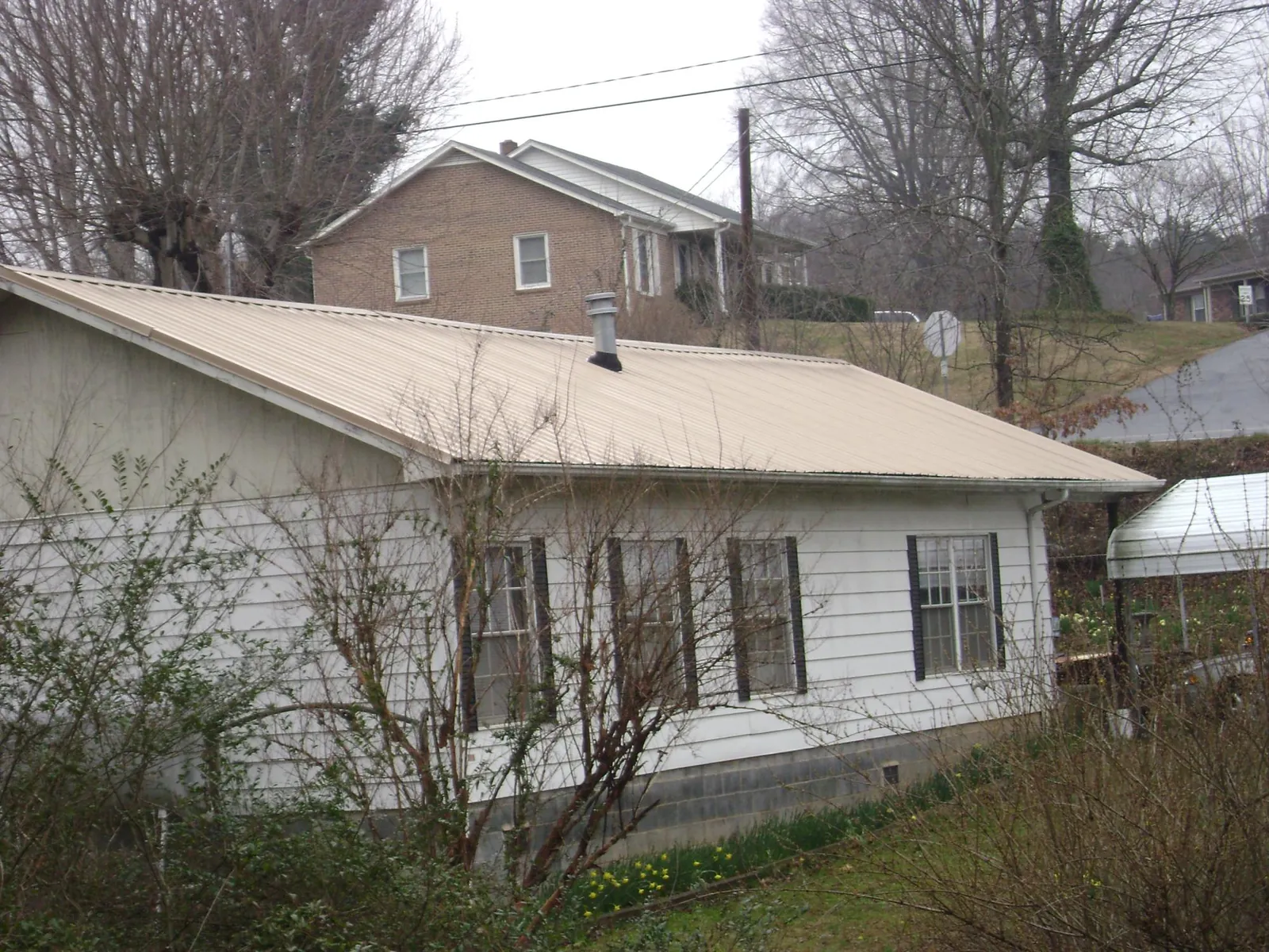 Tan metal roof on a white sided house set into a hillside — Commercial Roofing by Roofing Brothers in Dunfermline